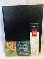 Lot contents showing a black hardcover sketchbook, Arteza 12-pack premium pencils box, and Cray-Pas Expressionist 12-color oil pastels box.
