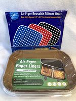 Photo displaying packaged air fryer reusable silicone liners and boxed air fryer paper liners stacked in front.