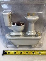 Full set of new porcelain doll house bathroom fixtures displayed in original clear plastic packaging with measuring tape showing scale.