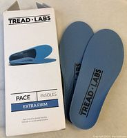 Photo showing the open box of Tread Labs Pace Extra Firm insoles alongside one insole laid flat to display design and shape.
