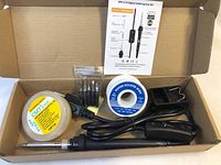 Top-down photo showing contents of the soldering iron kit inside the box. Includes soldering iron, power cord, solder wire spool, cleaning sponge, replacement tips, and soldering iron stand.