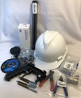 Photo showing all items in the lot including white hard hat, earplugs, drill bits, wire brushes, cutting disc, pliers, and other tools.