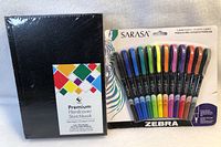 Photo showing black hardcover premium sketchbook and the full set of 12 Zebra Sarasa 0.8mm fine tip markers in original packaging.