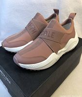 Side angle of new Kenneth Cole women's slip-on sneakers in muted pink with white soles on Kenneth Cole black box