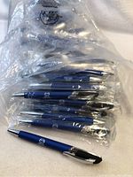 Blue pens with silver company logo, individually wrapped in clear plastic bags, showing side and top views of the pen with chrome accents.