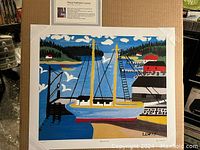 Full view of the print showing a colorful boat dock scene by Maud Kathleen Lewis on a cardboard backing with protective corner holders.