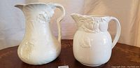 Photo showing two white porcelain antique pitchers side-by-side, highlighting their different shapes and relief decorations.