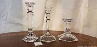 Front view of three crystal candlesticks of varying heights on a wooden surface with white cloth background.
