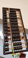 Front view showing the full abacus with beads in upper and lower sections along vertical rods in a dark wooden frame.
