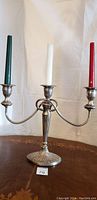 Full view of the antique English silver three-arm candelabrum with three taper candles (green, white, red) placed for scale and visual reference.