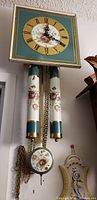 Full view of the antique French wall clock hanging with two weights and pendulum decorated with floral motifs.