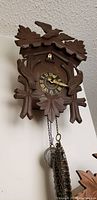Front view of antique wooden cuckoo clock showing carved leaves, birds, roman numeral dial, pendulum and weights.