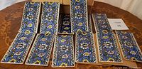 Set of 35 antique Persian blue porcelain tiles arranged on a table and a cardboard box, showing intricate floral design and overall quantity.