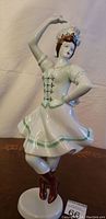 Full view of the porcelain figurine posed as a female dancer wearing traditional costume with skirt, bodice, and boots.