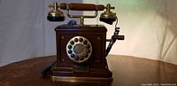 Front view of the antique Thomas telephone showing the rotary dial, brass cradle, and wooden handset.