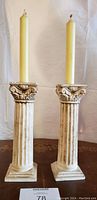 Full view of both antique stone column candlesticks holding tapered candles against a plain background.