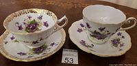 Two antique English porcelain teacups and saucers with violet floral pattern on wooden table