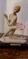 Side view showing ballerina figurine in light pink tutu on porcelain base, with orange hair and detailed facial features.