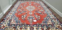 Full view of hand-made Kerman Persian rug laid flat showing red field and central medallion