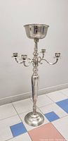 Front view of the full 43-inch tall silver plated candle holder with removable bowl on top, standing on tiled floor against white wall.