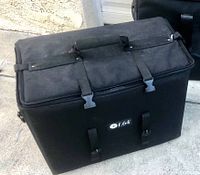 Black F.64 camera case exterior with two front strap closures and a top padded handle, shown on concrete surface.