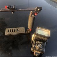 Both Stroboframe flash bracket and Vivitar 283 flash unit placed on flat surface under daylight.