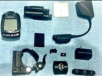 Full set of Cat Eye bicycle computer components including computer unit, sensor with connector, clamps, mounts, and small parts on a surface.