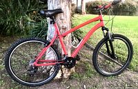 Side view showing red aluminum frame, black saddle, 26 inch wheels with knobby tires, Shimano drivetrain components