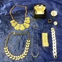 Full lot of fashion jewelry items arranged on blue fabric, including necklaces, rings, bracelets, and a brooch.