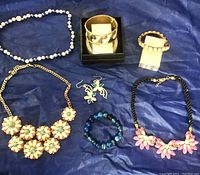 Photo of lot showing multiple pieces of fashion jewelry including necklaces, bracelets, earrings, and rings on a blue fabric surface.