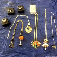 Overview of all jewelry pieces laid on blue fabric, including rings on stands, necklaces laid flat showing unique pendants, and earrings in box