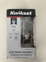 Front view of Kwikset electronic deadbolt in original box with branding and product name visible.