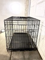 Angle showing the large black metal wire dog crate with one visible door and a removable bottom tray inside.