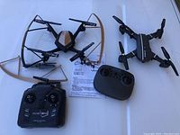 Lot contains two drones and their remote controllers with accessories arranged on a white surface.