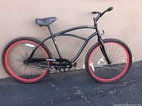 Side view of black Phat cruiser bike with red rims and curved frame from the right side.