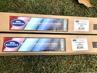 Two Savage brand seamless background paper rolls in cardboard packaging. Labels show one roll as White and the other as Fashion Gray, both 86 inches by 12 yards.