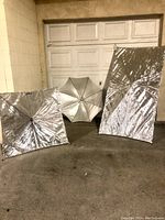 Lot of three photography lighting reflectors: one umbrella reflector, one square reflector, one rectangular reflector, all silver.