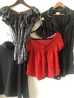 Four women's clothing items hung on hangers: charcoal gray ruffled blouse, striped black and gray top, red off-shoulder blouse, black pinstripe blazer