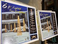 Boxes of two 6ft Lighted Tree Sculptures showing product images and details, including spiral design, star topper, white mini lights, UL listing, and accessories.