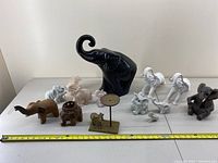 Full view of all 12 elephant figurines arranged in front of a white background with tape measure for scale
