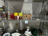 Shelf with various barware including colored goblets, shot glasses, whiskey stones set, empty cognac box, and different glassware.