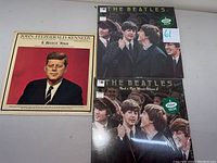 John F Kennedy Memorial Album and two Beatles Rock n Roll Music Volume 1 and 2 albums on flat surface
