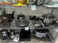 Wide shot of shelf displaying multiple pots, pans, induction cooktop, and related cookware with item tags.