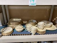 Shelf with the dishware set displayed including stacks of plates, tea cups, saucers, and a sugar bowl showing gold leaf edges and Nautilus shell pattern with floral accents.