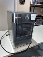 Front and side view of the GE Profile ice maker machine showing stainless steel and black housing with plug-in cord visible.
