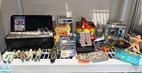 Full lot overview including Ghostbuster figures, trading card box, Disney Pop, Curious George metal box, Pet Pup night light, Hot Wheels cars, and small miscellaneous items on a table