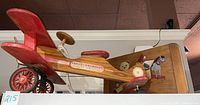 Side view of large wooden red airplane pull toy with decals, showing vintage wheels and propeller.