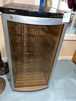 Front view of Haier wine fridge showing tinted clear door with seven internal wine racks, black and stainless steel body.