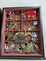 Photo showing large assortment of vintage costume jewelry including various pins, brooches, earrings, rings, and pendants arranged in a sectioned tray.