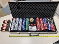 Open metallic briefcase poker set showing multiple stacks of white, blue, green, red, black chips, and a dealer chip with foam padding inside lid